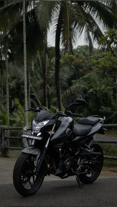 a black motorcycle parked in front of some palm trees and other greenery behind it