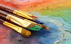 three paintbrushes sitting on top of a table covered in multicolored paints