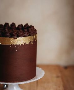 a chocolate cake with gold frosting on a white plate sitting on a wooden table