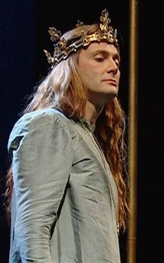 a man with long hair wearing a crown on his head and standing in front of a pole