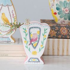 two vases sitting on top of books next to each other with flowers and birds painted on them