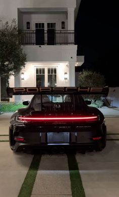 a car parked in front of a house at night with its lights on and the roof down