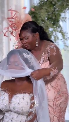 two women dressed in pink and white, one is holding a veil over the other's head