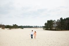 a man and woman walking across a sandy beach