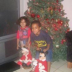 two children sitting in front of a christmas tree with mickey mouses on the floor