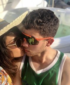 a young man and woman are kissing on the beach while wearing sun glasses, one is holding his face to the other's chest