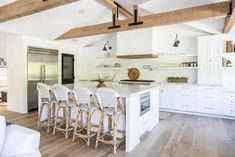 a large kitchen with white cabinets and wooden beams on the ceiling, along with bar stools