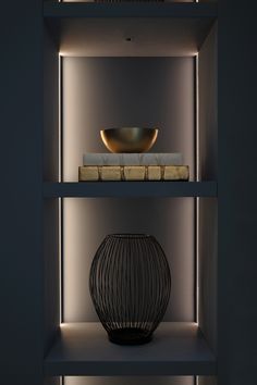 a black vase sitting on top of a shelf next to a bowl and bookcase