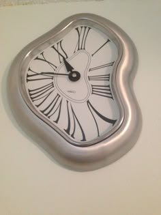 a silver clock with black and white designs on it's face is hanging from the wall