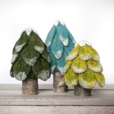 three small trees made out of felt sitting on top of a wooden table next to each other