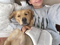 a woman laying in bed next to a dog with an open book on her lap