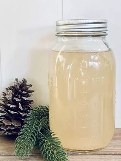 a pine cone is next to a jar of liquid on a wooden table with fir cones