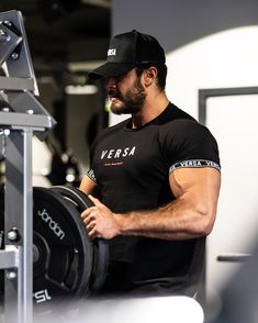 a man in a black shirt and hat working out with a barbell machine at the gym