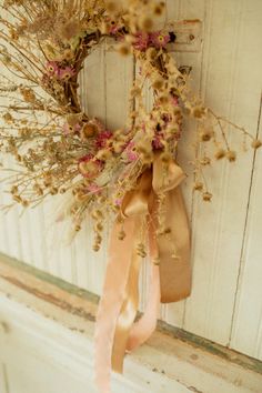 a wreath hanging on the side of a door with flowers and ribbons attached to it