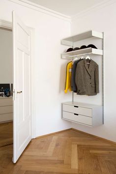 an open closet with clothes and shoes on shelves next to a white door that leads to another room