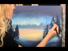 a woman is painting a snowy scene with trees