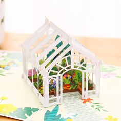 a small white house sitting on top of a table next to a potted plant