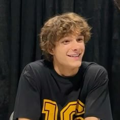 a young man sitting in front of a black curtain