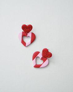 two red and pink heart shaped brooches sitting on top of a white surface