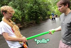 two young men are holding green hoses in the street