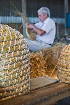 a man sitting on a bench next to baskets filled with grass and other items in front of him