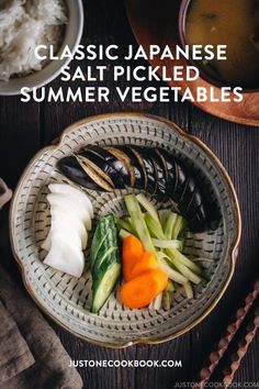 a bowl filled with assorted vegetables next to rice and chopsticks on a wooden table