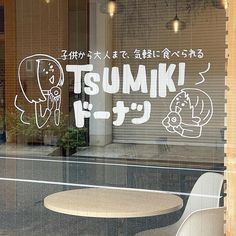 a table and chair in front of a store window with writing on the glass that says tumiki