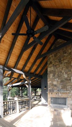 an outdoor covered patio with stone fireplace and ceiling fan, surrounded by wood planks