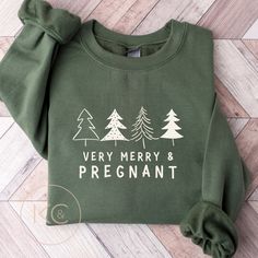 a green sweatshirt that says very merry and pregnant on the front with trees around it