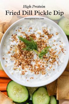 a white bowl filled with dip surrounded by cucumbers and crackers on top