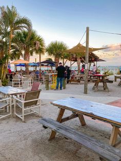 tables and umbrellas are set up on the beach for an outdoor dining area at sunset