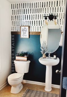 a white toilet sitting next to a sink in a bathroom under a mirror and wallpaper