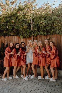 a group of women standing next to each other near a wooden fence and tree with flowers