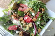 a salad with spinach, strawberries, nuts and feta cheese on it