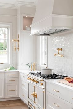 a kitchen with white cabinets and gold trim on the stove top, along with brass pulls