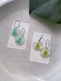 two earrings are sitting on a plate next to a plant