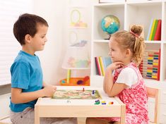 two children sitting at a table playing with a board game on the floor in front of bookshelves