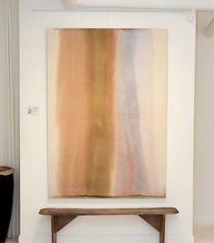 an abstract painting hangs on the wall next to a wooden bench in a white room