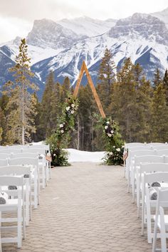 an outdoor ceremony setup with white chairs and floral arch in front of snowy mountain backdrop