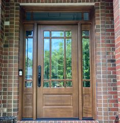 a wooden front door with glass panels and sidelights on brick wall next to bench