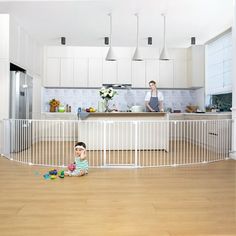 a young child sitting on the floor in front of a kitchen with an adult standing behind it