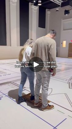 a man and woman standing on top of a skateboard in a room with white walls