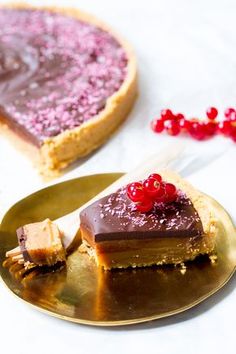 a piece of cake on a gold plate next to a slice of pie with chocolate and raspberry toppings