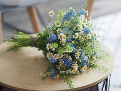 a bouquet of wildflowers and daisies on a wooden table with chairs in the background