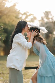 two women are kissing each other in front of the grass and trees, one is wearing a blue dress