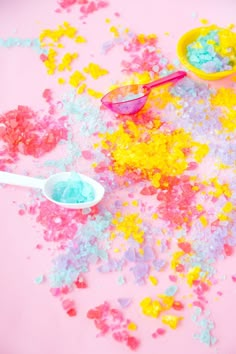 colorful confetti spilled on top of a pink surface with two plastic spoons