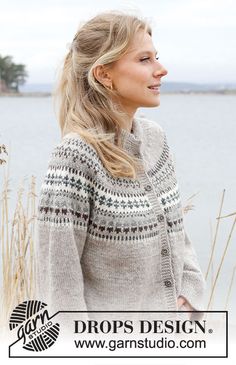 a woman standing by the water wearing a sweater