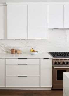 a kitchen with white cabinets and marble counter tops, an oven and stove top in the center