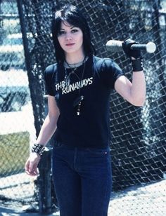 a woman with black hair holding a tennis racquet in her right hand and standing next to a chain link fence