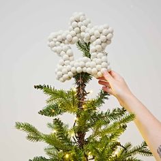 someone is holding balls on the top of a christmas tree with lights around it and they are white